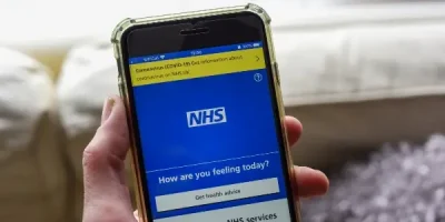 Person holding phone displaying NHS COVID-19 information page